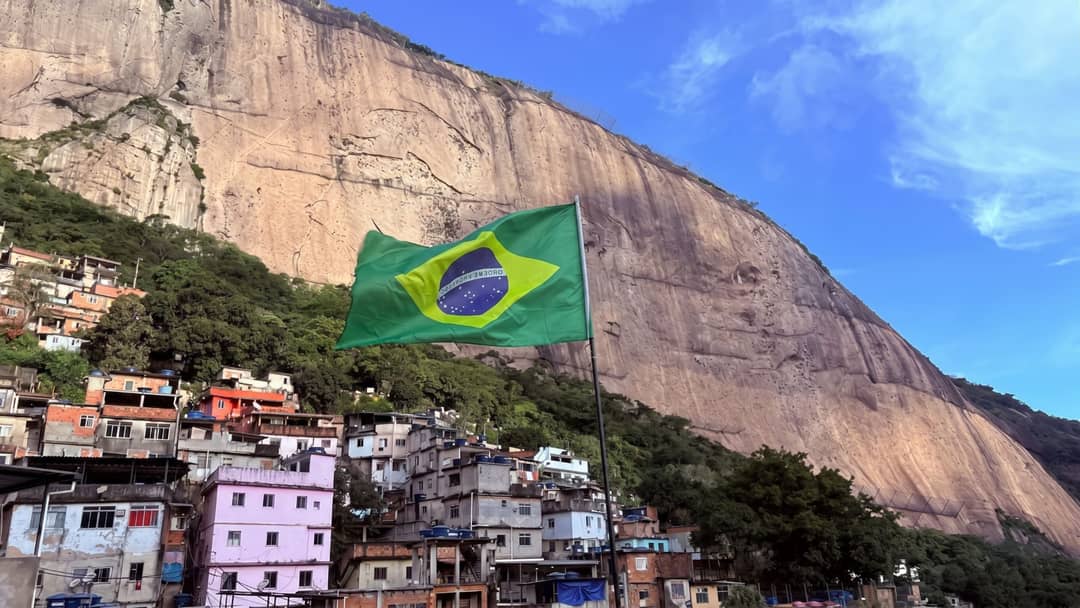 Bandeira do Brasil numa laje da favela, com casas coloridas e um paredão de pedra ao fundo